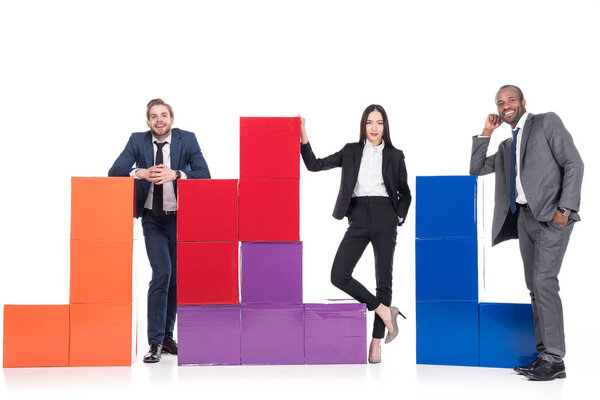 улыбающиеся многонациональные бизнесмены, стоящие рядом с красочными блоками, изолированными по белой концепции командной работы
