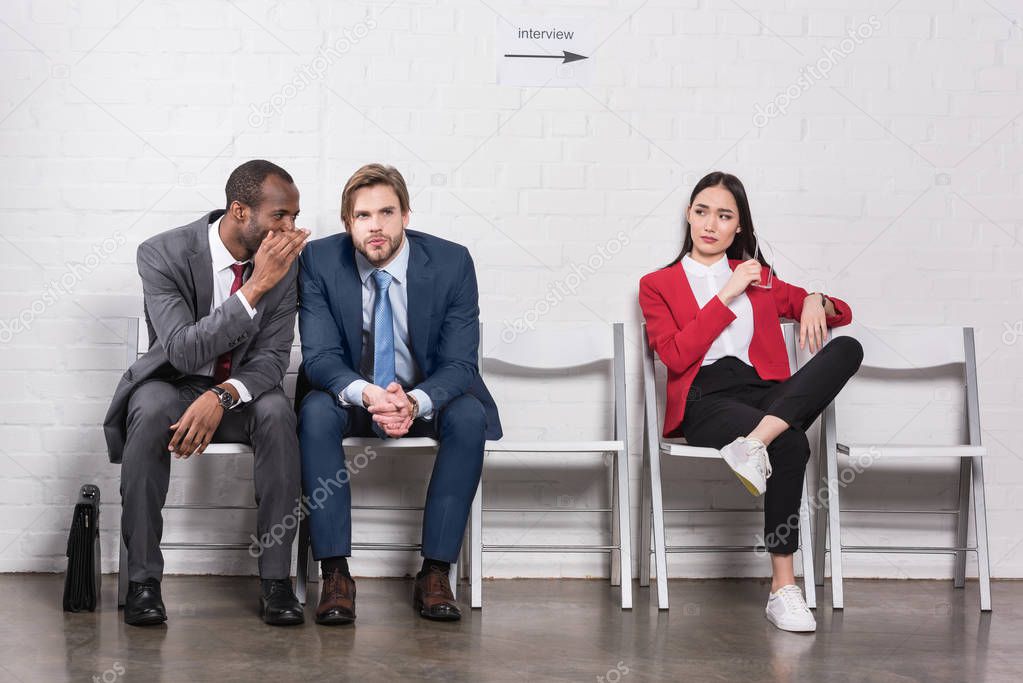 asian businesswoman looking at multicultural businessmen gossiping while waiting for job interview