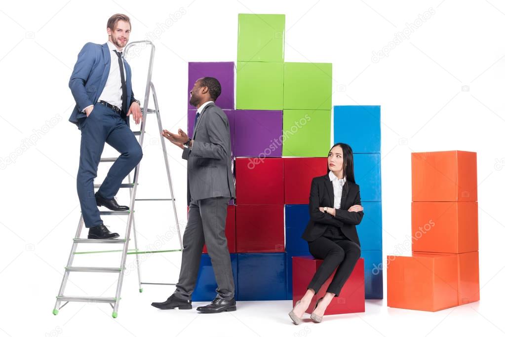 asian businesswoman looking at multicultural businessmen having conversation near colorful blocks isolated on white