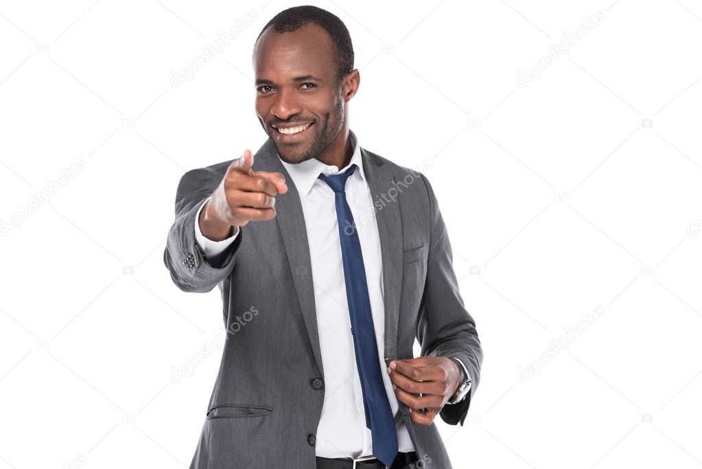 portrait of smiling african american businessman pointing at camera isolated on white