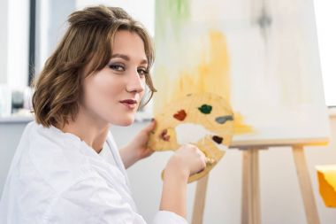 Young artistic girl mixing paint in light studio clipart