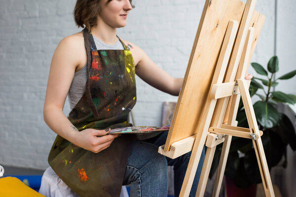 Молодая художница рисует на холсте в светлой студии
