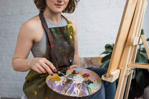 Close-up view of young creative girl with painting knife in light studio