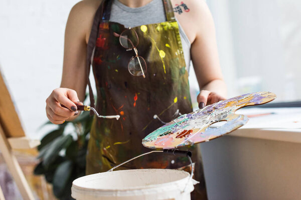 Close-up view of young inspired girl working with painting knife and palette in light studio