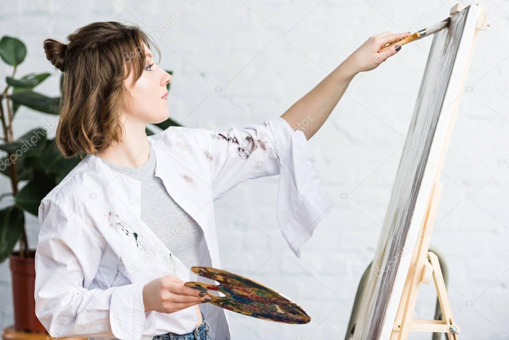 Young creative girl smears paint on canvas in light studio