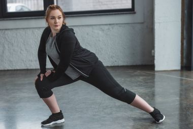 Overweight girl stretching legs in gym