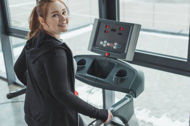 Curvy kız spor salonunda ise koşu bandı üzerinde gülümseyen
