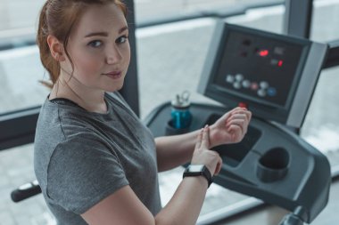 Genç kız spor salonunda koşu bandı üzerinde çalışma sırasında nabız kontrol