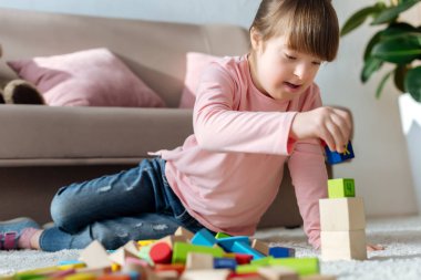Child with down syndrome playing with toy cubes on floor in cozy room clipart