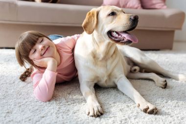 Happy child with down syndrome lying on the floor with Labrador retriever  clipart