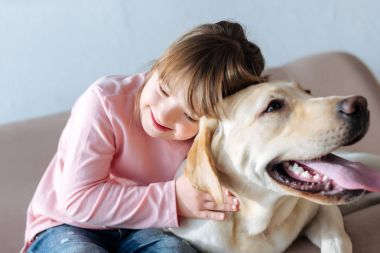 Down sendromu ve Labrador retriever köpek kanepede sarılma ile mutlu çocuk