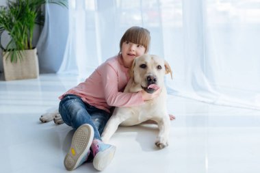 Child with down syndrome embracing Labrador retriever lying on the floor