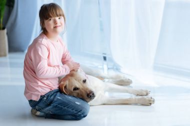 Kid with down syndrome stroking Labrador retriever dog and looking at camera clipart