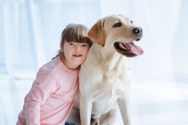 Kid girl with down syndrome embracing Labrador retriever on light background clipart