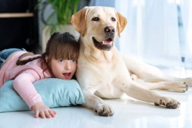Kid with down syndrome lying on the floor next to Labrador retriever dog clipart