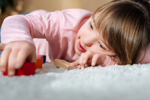 床の上に横たわっている間おもちゃキューブで遊んでダウン症子供します — ストック写真