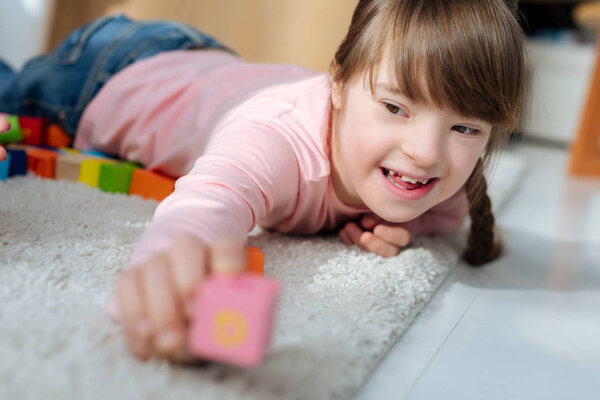 Ребенок с синдромом Дауна держит игрушечный куб
