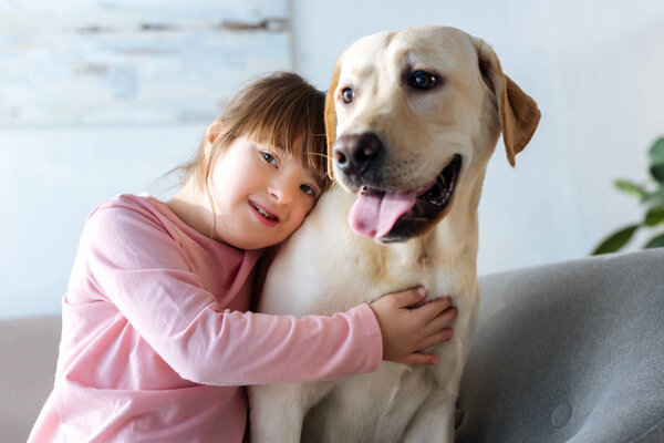Child with down syndrome embracing Labrador retriever and looking at camera