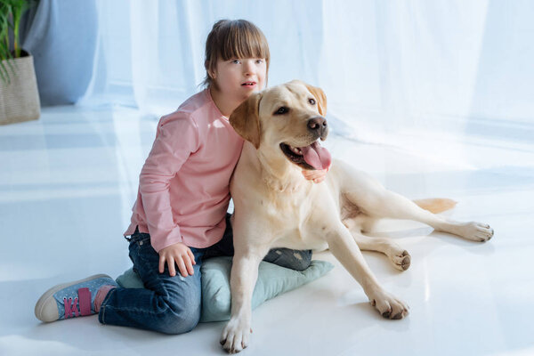 Ребенок с синдромом Дауна возле собаки Лабрадора на полу
