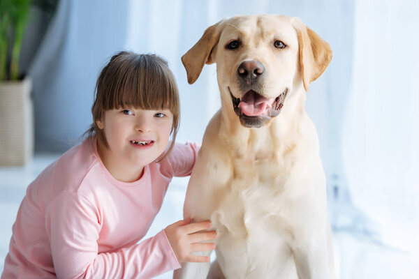 Happy child girl with down syndrome cherishing Labrador retriever 
