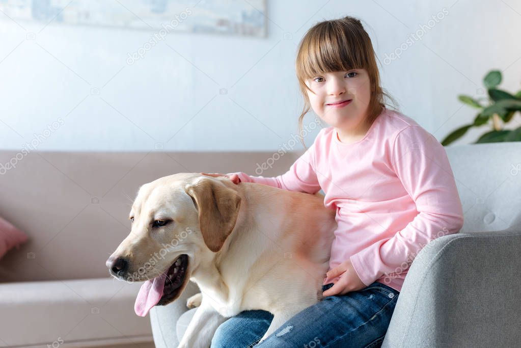 Kid with down syndrome and Labrador retriever sitting in chair