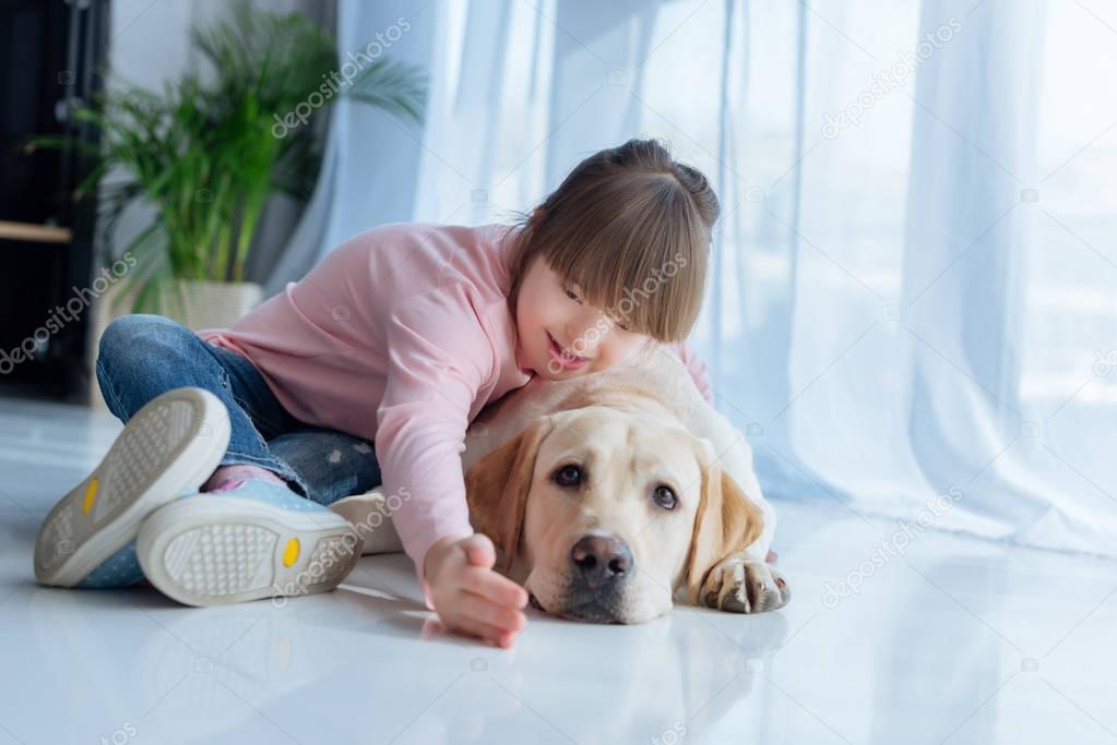 Child with down syndrome playing with Labrador retriever dog on the floor