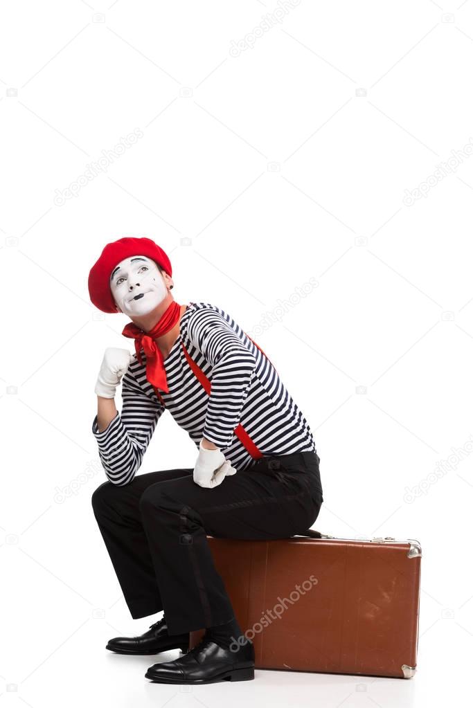 pensive mime sitting on brown suitcase isolated on white