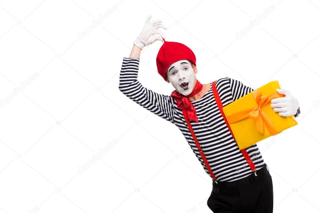 surprised mime holding gift box and touching red cap isolated on white
