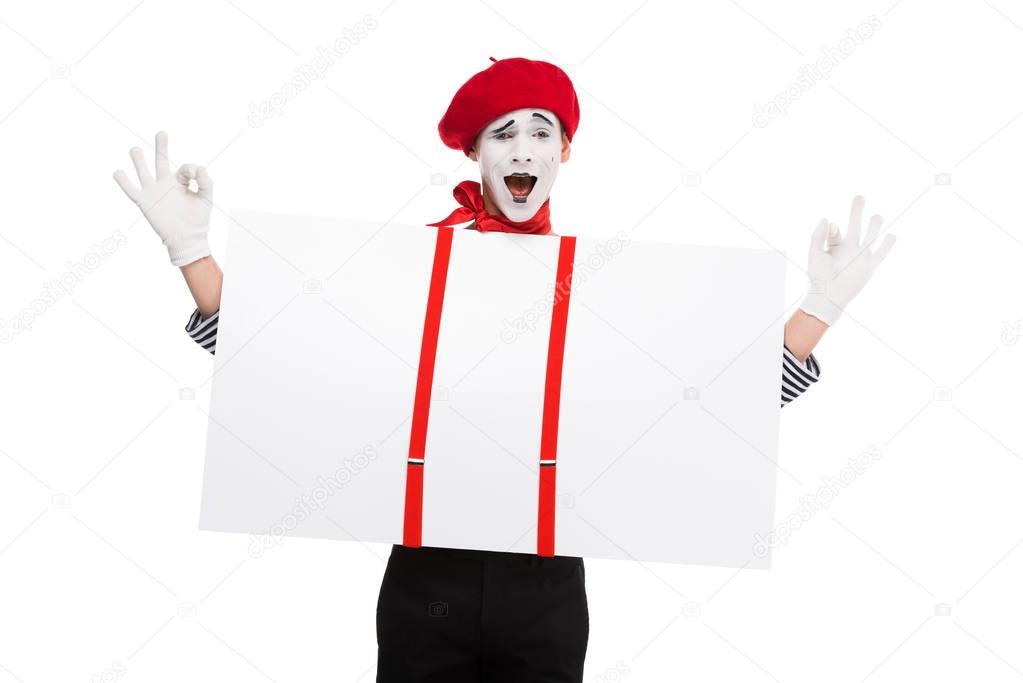 happy mime holding empty board under suspenders and showing ok sign isolated on white