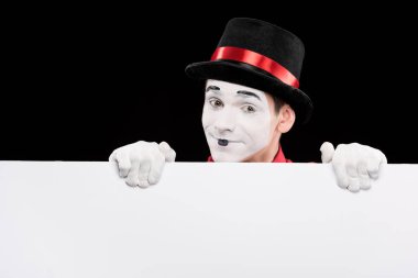 happy mime looking out from empty board isolated on black clipart