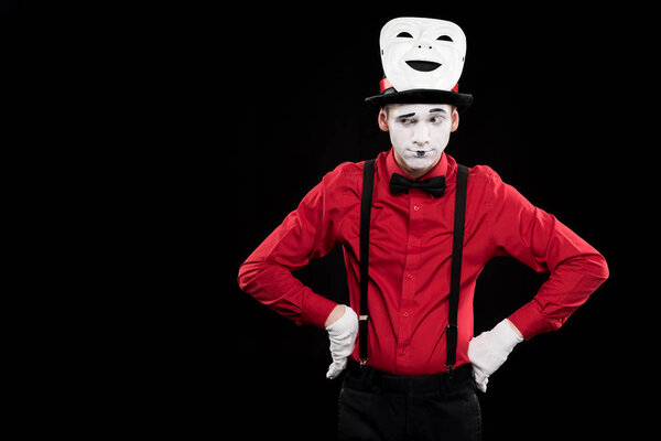 grimacing mime with hands akimbo and mask on hat isolated on black