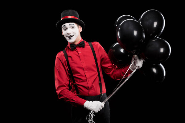 smiling mime holding bundle of black balloons isolated on black