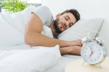 handsome bearded man sleeping in bed in the morning, alarm clock on foreground clipart