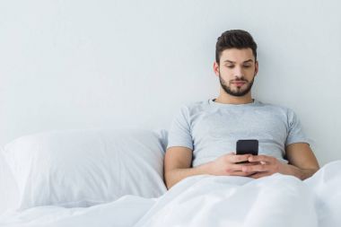 yatakta yatarken ve Smartphone'da mesajlaşma sakallı adam