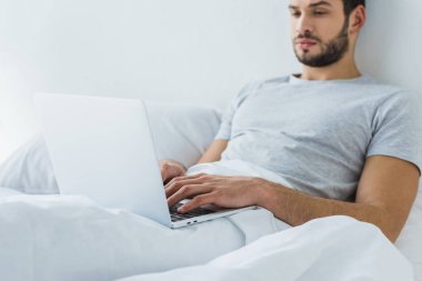 yatakta yatarken ve dizüstü bilgisayar kullanarak sakallı adam