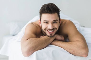 Beyaz yatakta yatarken ve kameraya bakarak yakışıklı neşeli s adam