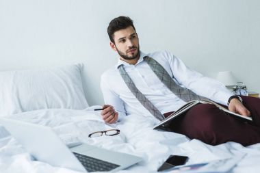 belgeler ve dijital cihazlar ile yatakta yatarken işadamı