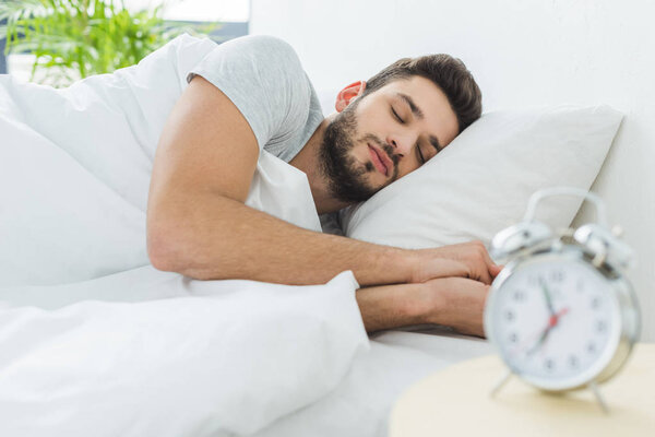 handsome bearded man sleeping in bed in the morning, alarm clock on foreground