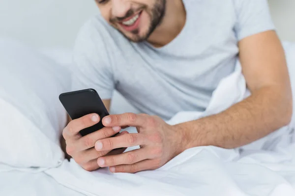 Homme Barbu Souriant Couché Sur Lit Utilisant Smartphone — Photo gratuite