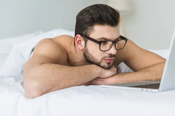 戴眼镜的英俊胡子男子在床上看膝上型电脑 — 图库照片