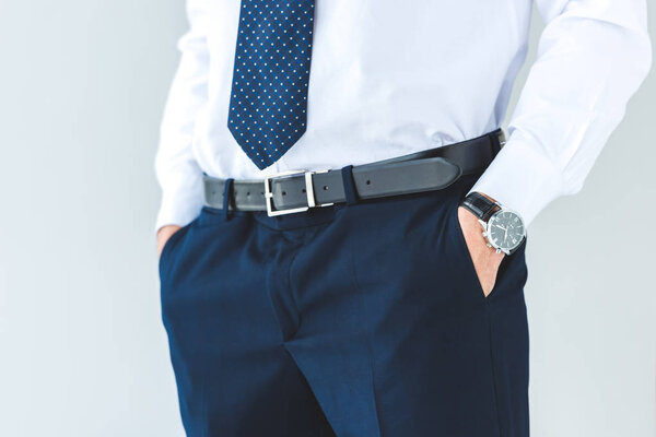 cropped view of businessman with hands in pockets, isolated on grey