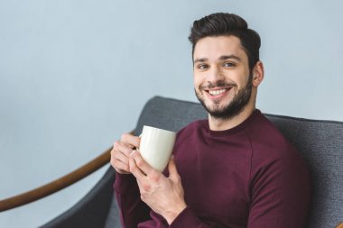 mutlu yakışıklı Kupası içki ile tutarak ve koltukta oturan adam sakallı