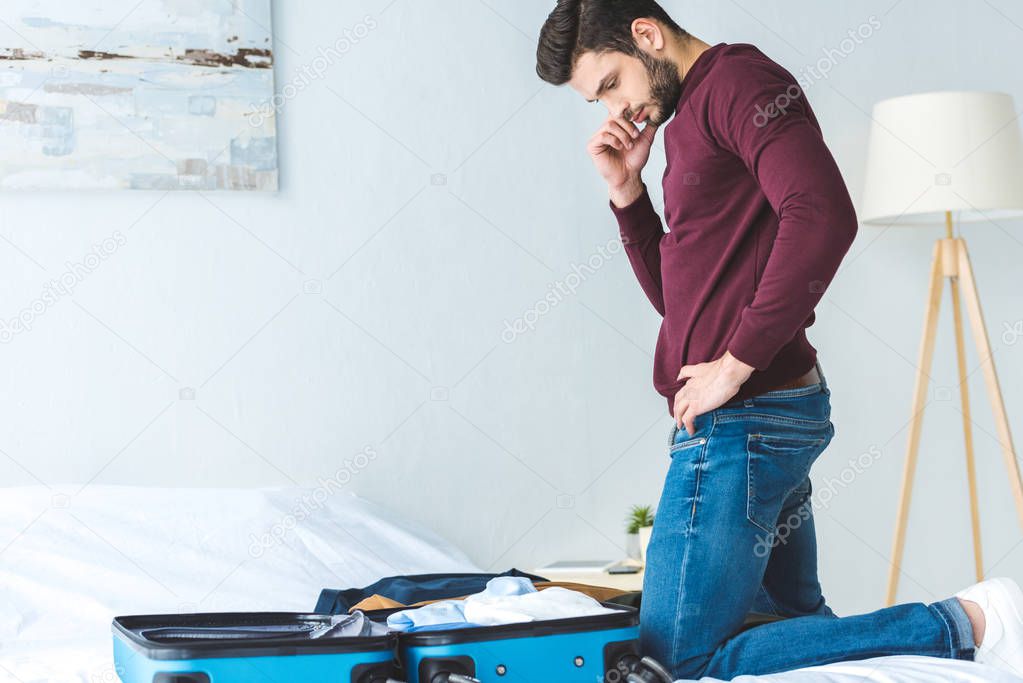 thoughtful young man packing luggage on bed for travel