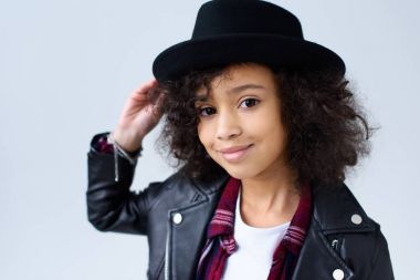 close-up portrait of adorable little child in leather jacket and hat looking at camera isolated on grey clipart