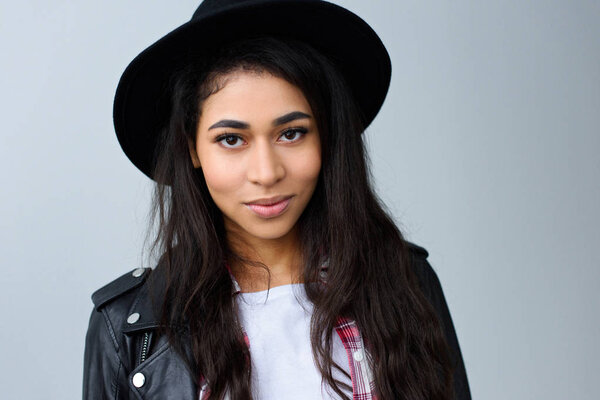 крупным планом портрет улыбающейся молодой женщины в шляпе, смотрящей в камеру, изолированную на сером
