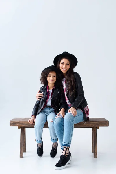 时尚的年轻母亲和女儿在类似的衣服坐在板凳上一起孤立的灰色 — 图库照片