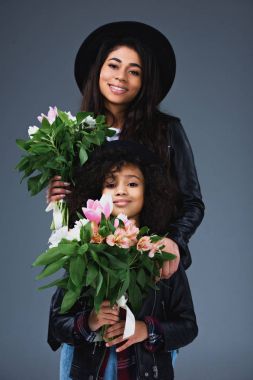beautiful mother and daughter in leather jackets and hats with beautiful bouquets isolated on grey clipart