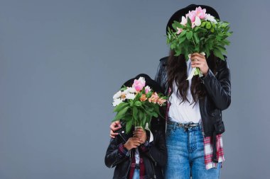mother and daughter covering faces with bouquets isolated on grey clipart