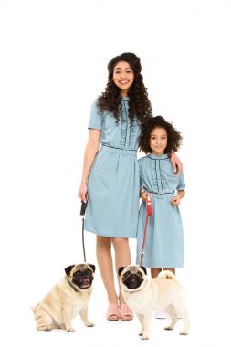 happy mother and daughter in similar dresses with pugs on leashes isolated on white clipart