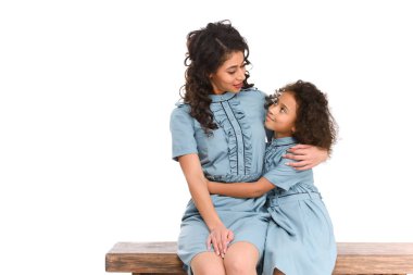 mother and daughter embracing while sitting on bench isolated on white clipart